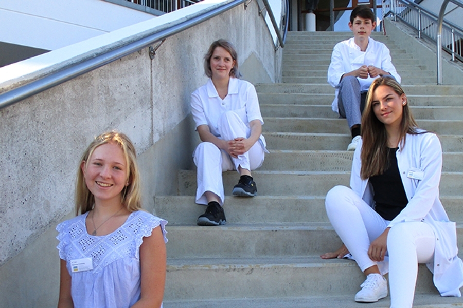 Mehrere Auzubildende sitzen lächelnd auf einer Treppe Mehrere Auzubildende sitzen lächelnd auf einer Treppe