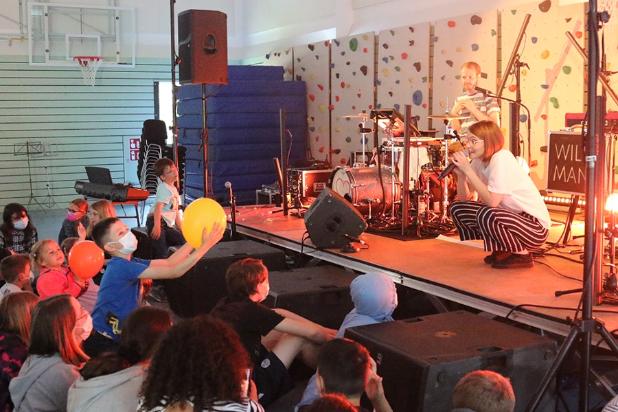 Eine Band steht auf einer Bühne und musiziert für ihr junges Publikum.