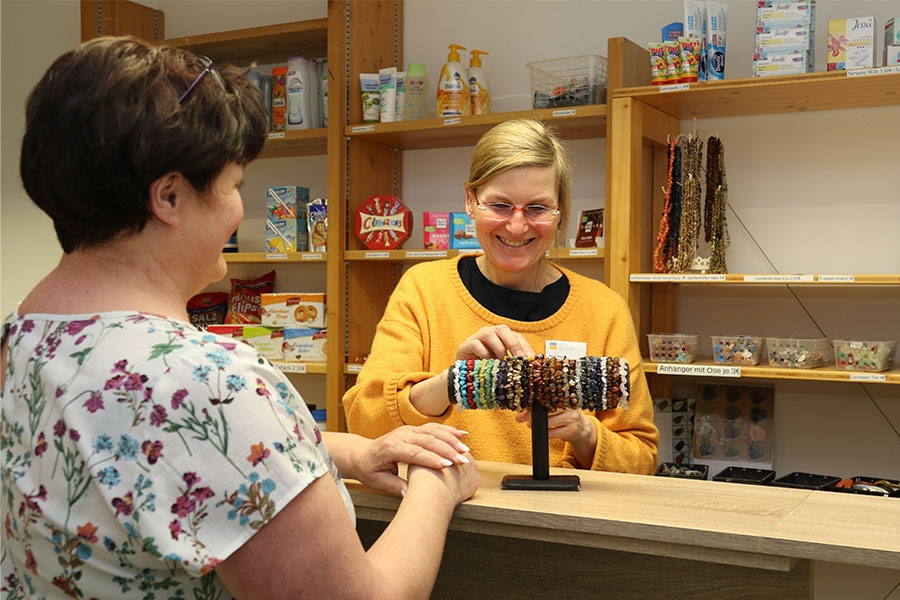 Eine Verkäuferin steht hinter dem Tresen des Klinik-Kiosk und greift zu einem Schmuckarmband. Eine Verkäuferin steht hinter dem Tresen des Klinik-Kiosk und greift zu einem Schmuckarmband.