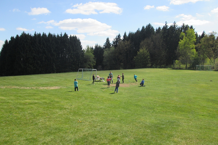 Eine Kindergruppe spielt auf großer Rasenfläche Fußball.