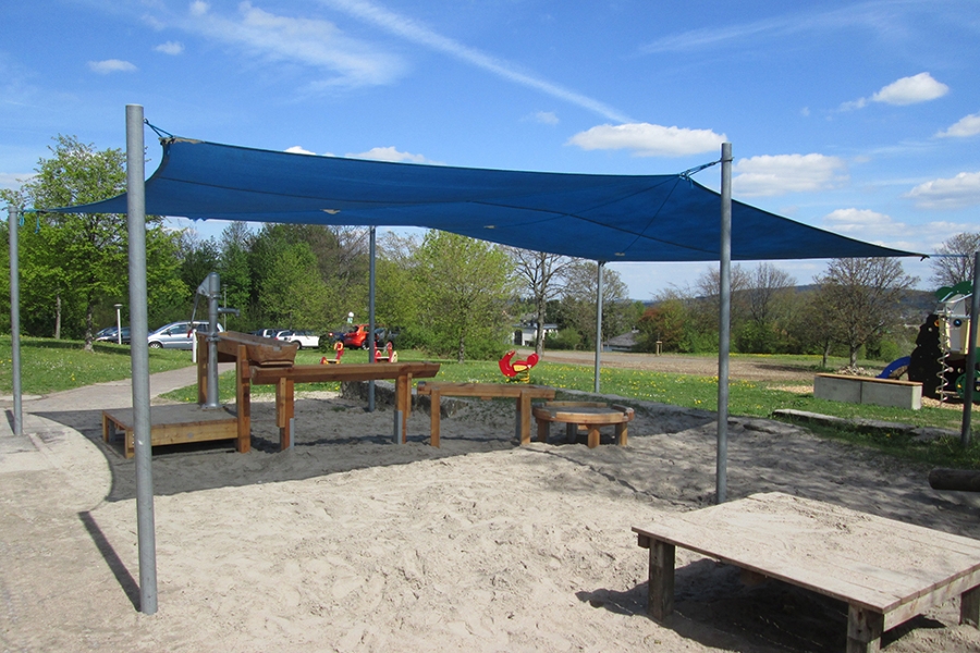 Ein Sonnendach spendet Schatten über einem Sandspielbereich. Ein Sonnendach spendet Schatten über einem Sandspielbereich.