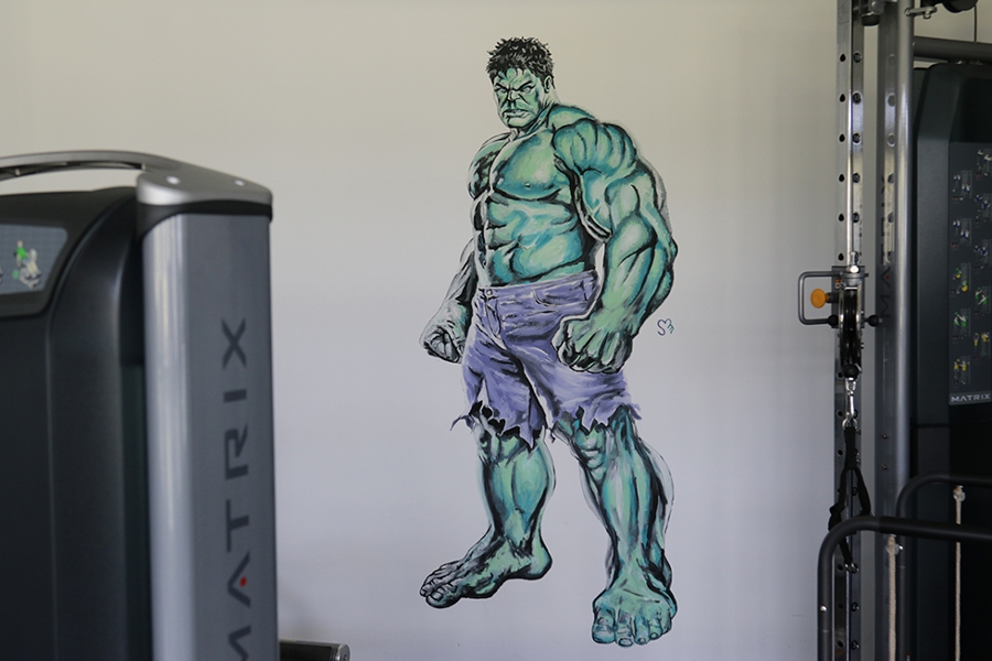 Zwischen zwei Sportgeräten befindet sich an der Wand ein Wandtattoo vom Hulk.