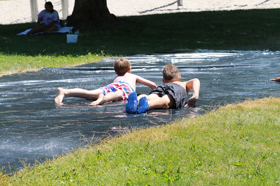 Zwei Kinder rutschen auf einer Wasserrutsche auf dem Rasen. Zwei Kinder rutschen auf einer Wasserrutsche auf dem Rasen.