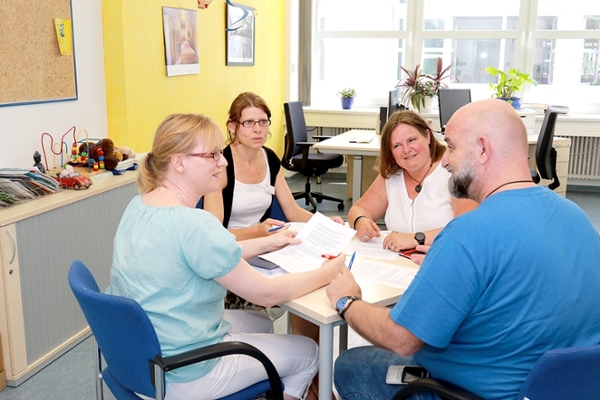 Drei Frauen und ein Mann sitzen um einen Tisch herum und tauschen sich aus. Drei Frauen und ein Mann sitzen um einen Tisch herum und tauschen sich aus.