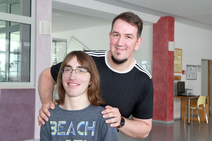 Ein Physiotherapeut steht hinter Philipp, einem Patienten, und legt seine Hände auf dessen Schultern. Ein Physiotherapeut steht hinter Philipp, einem Patienten, und legt seine Hände auf dessen Schultern.