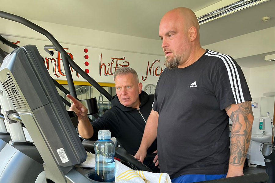 Ein Therapeut weist einen Mann am Laufband ein Ein Therapeut weist einen Mann am Laufband ein